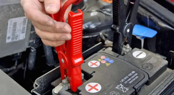 Starthilfe geben Anleitung: Rote Klemme wird an Autobatterie befestigt.