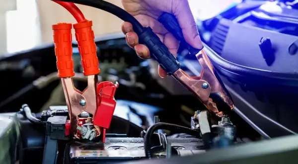 Eine Hand gibt Starthilfe, indem sie ein Überbrückungskabel an der Autobatterie befestigt.
