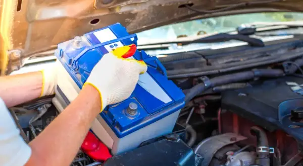 Person mit Handschuhen tauscht eine Autobatterie aus. Dies kann helfen, schwache Batterie Symptome wie Startschwierigkeiten zu beheben.