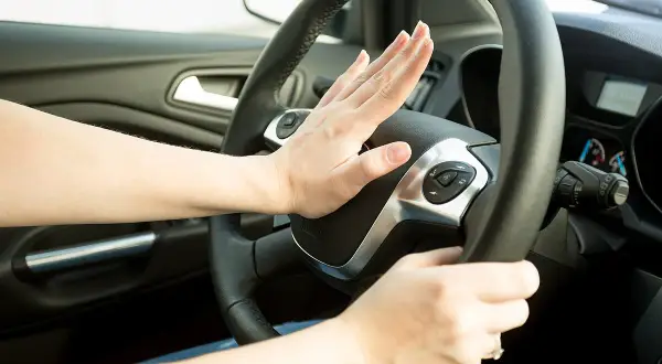 Hand drückt Hupe im Auto. Innerorts darf die Hupe nur zur Warnung vor Gefahren oder beim Überholen verwendet werden.