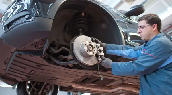 Mechaniker prüft Bremsen eines Autos. Das Quietschen der Bremsen kurz vor Stillstand ist ein Warnsignal für Verschleiß.