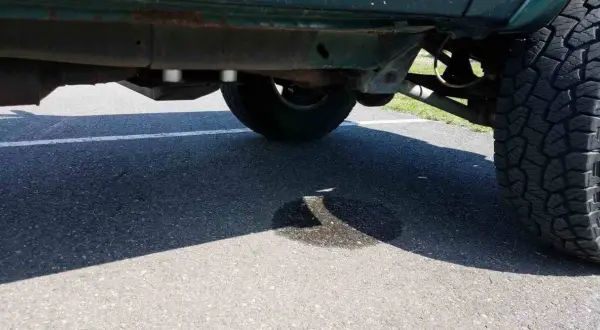 Ein Auto tropft Wasser nach der Fahrt. Eine Pfütze bildet sich auf dem Asphalt unter dem Fahrzeug.