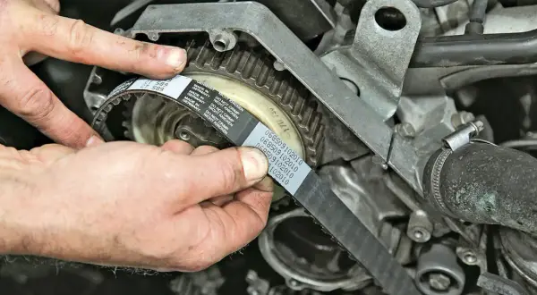 Hände montieren einen neuen Zahnriemen am Motor. So gelingt der Zahnriemenwechsel selbst.