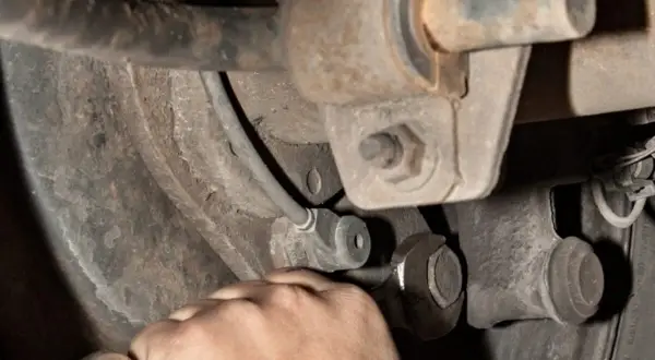 Hand mit Schraubenschlüssel am Auto-Fahrwerk. Mögliche stabilisator auto defekt symptome wie Klappern sind hier zu beheben.