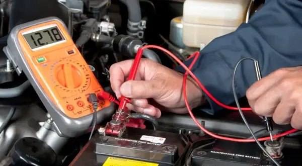 Mechaniker prüft Autobatterie mit Multimeter. Mögliche Symptome eines defekten Magnetschalters werden untersucht.