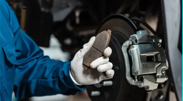 Mechaniker hält abgefahrene Bremsen in der Hand, bereit für den Austausch.