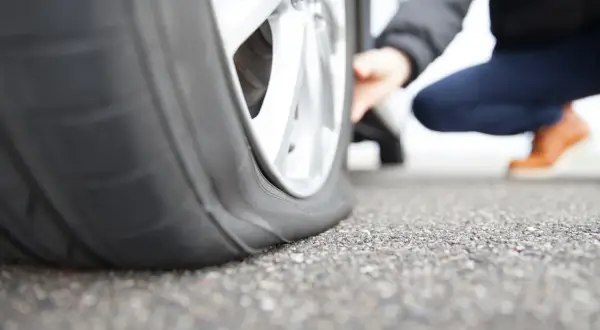 Platter Reifen am Auto. Eine Person kniet daneben und prüft den Schaden. Was tun bei reifen platt?