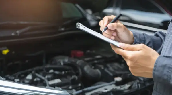 Mechaniker prüft mit Klemmbrett und Stift den Motorraum. Dies ist wichtig für die Betriebssicherheit des Autos.