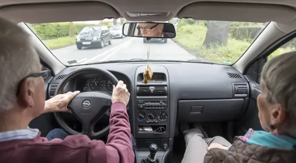 Älteres Paar im Auto. Der Fahrer hält das Lenkrad, während das Auto vibriert beim Bremsen. Die Beifahrerin schaut nach vorne.
