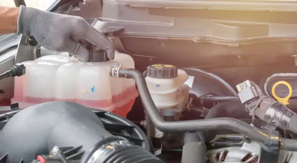 Hand in glove checks the coolant level in the car's engine. The pink liquid is the **wasser unter auto**, essential for keeping the engine cool.
