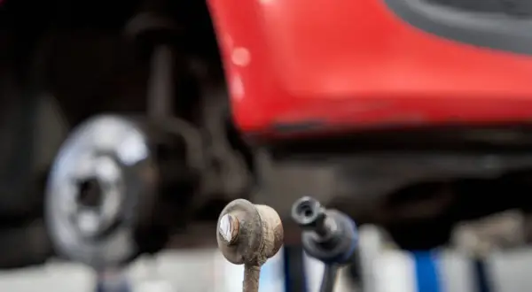 Zwei Koppelstangen liegen vor einem roten Auto. Die Koppelstange ist ein wichtiges Bauteil für die Fahrstabilität.
