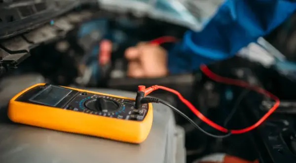 Ein Mechaniker testet die auto batterie mit einem Multimeter. Das gelbe Gerät liegt auf dem Motorraum.