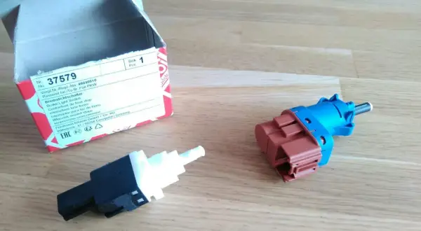 Zwei neue Bremslichtschalter liegen neben einer geöffneten Verpackung. Ein Teil ist blau und braun, das andere schwarz und weiß.