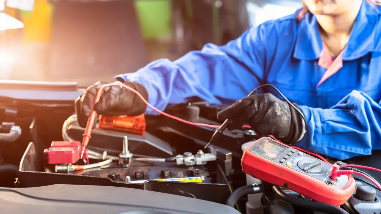 Mechaniker prüft mit Multimeter eine Autobatterie. Möglicherweise ist die **Batterie defekt**.
