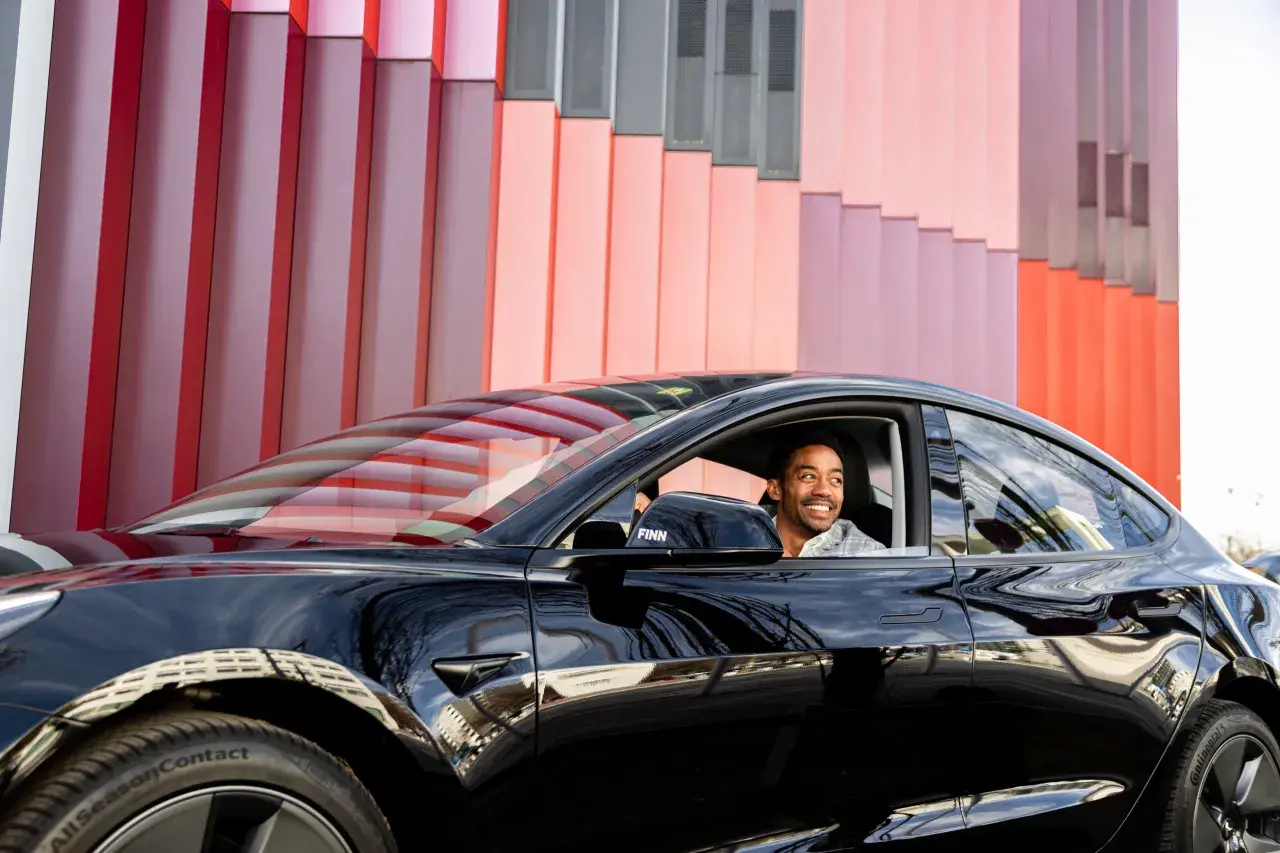 Mann lächelt im schwarzen Auto vor bunter Fassade. Ein guter Deal, der Bruttolistenpreis mit Rabatt macht es möglich.