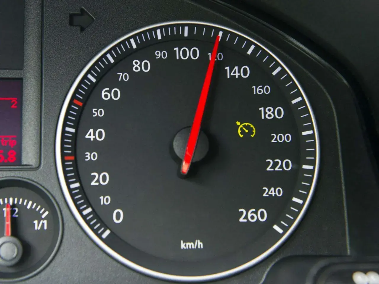 Tacho zeigt 100 km/h. Die gelbe Warnleuchte mit Uhr deutet auf eine mögliche Tacho-Toleranz oder Geschwindigkeitsbegrenzung hin.
