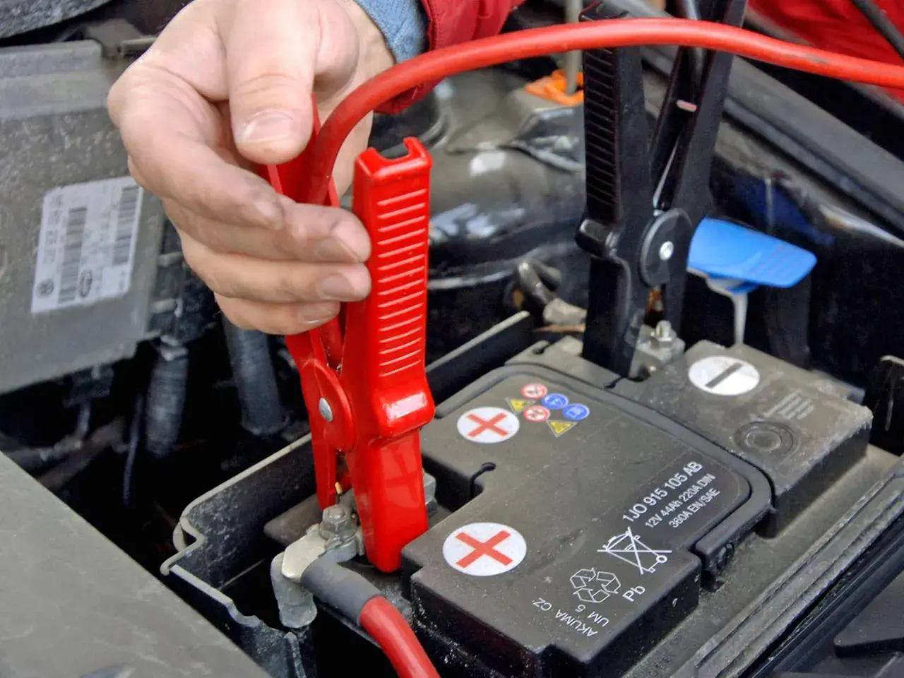Starthilfe geben Anleitung: Rote Klemme wird an Autobatterie befestigt.