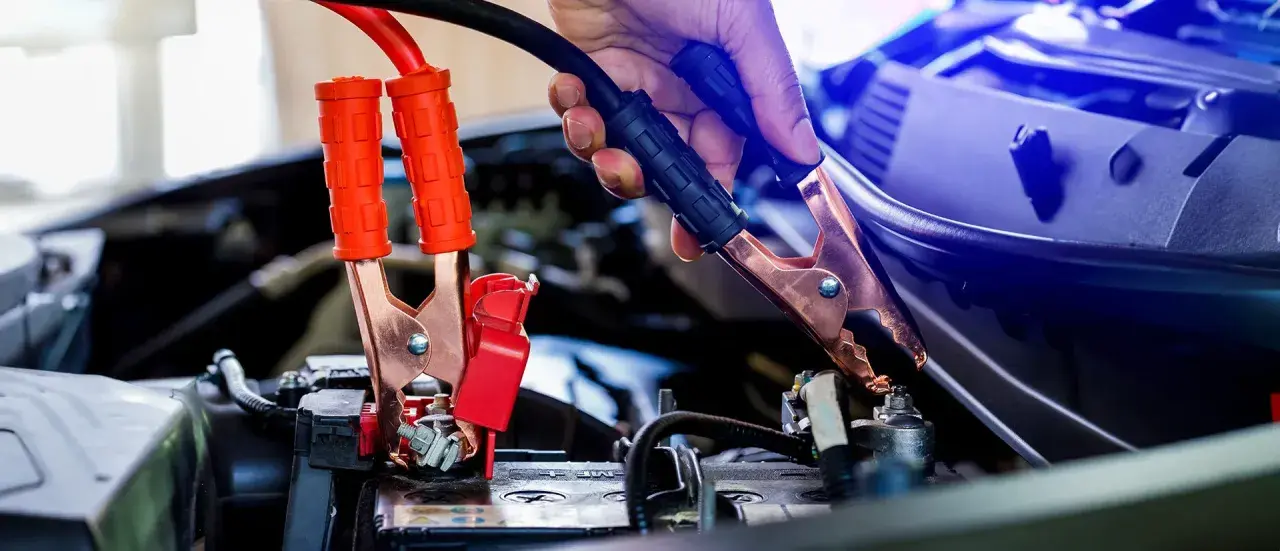 Eine Hand gibt Starthilfe, indem sie ein Überbrückungskabel an der Autobatterie befestigt.