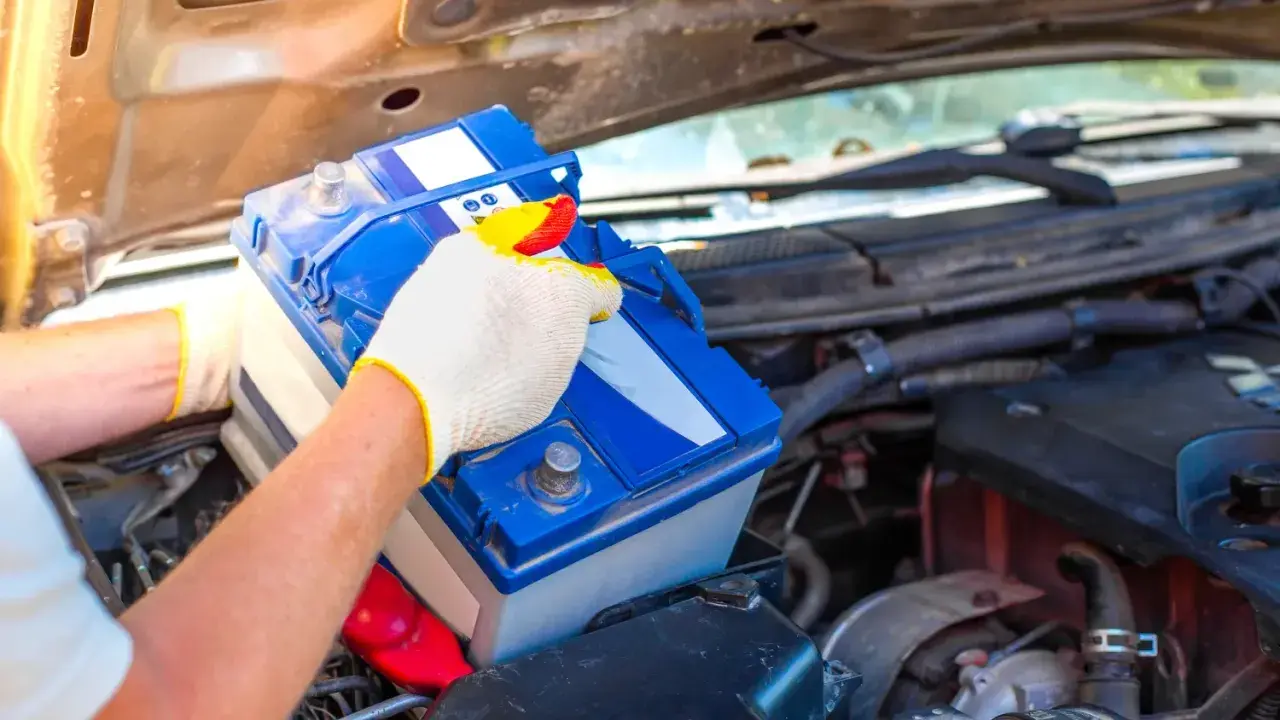 Person mit Handschuhen tauscht eine Autobatterie aus. Dies kann helfen, schwache Batterie Symptome wie Startschwierigkeiten zu beheben.