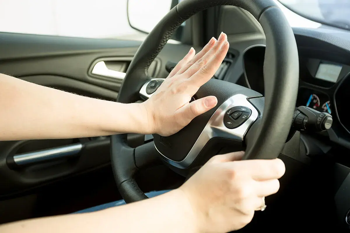 Hand drückt Hupe im Auto. Innerorts darf die Hupe nur zur Warnung vor Gefahren oder beim Überholen verwendet werden.
