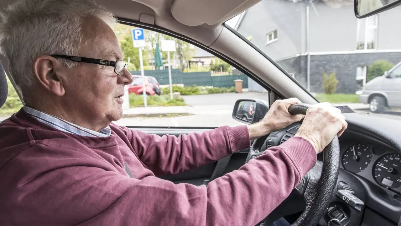 Älterer Mann fährt Auto, das beim Fahren quietscht. Er blickt konzentriert auf die Straße.