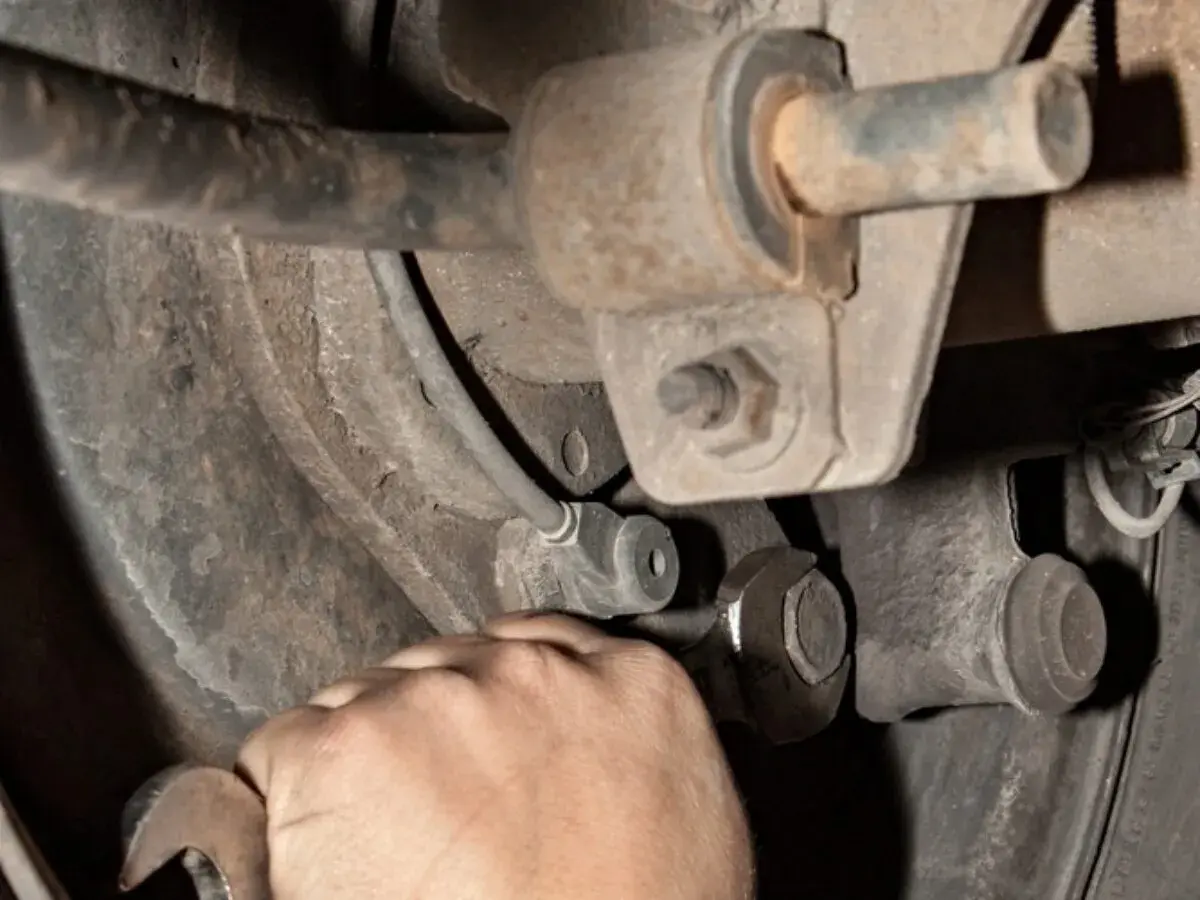 Hand mit Schraubenschlüssel am Auto-Fahrwerk. Mögliche stabilisator auto defekt symptome wie Klappern sind hier zu beheben.