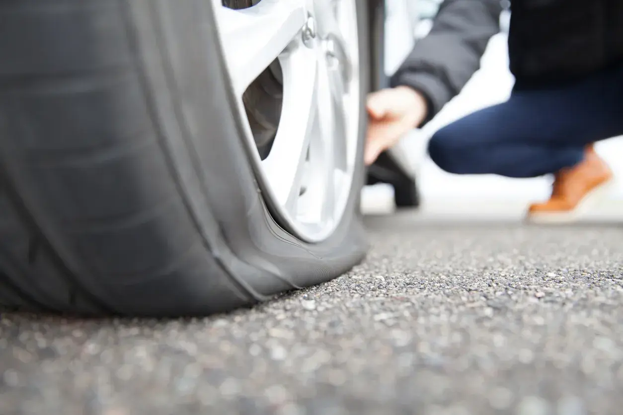 Platter Reifen am Auto. Eine Person kniet daneben und prüft den Schaden. Was tun bei reifen platt?