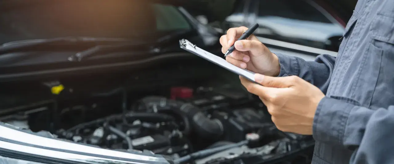 Mechaniker prüft mit Klemmbrett und Stift den Motorraum. Dies ist wichtig für die Betriebssicherheit des Autos.
