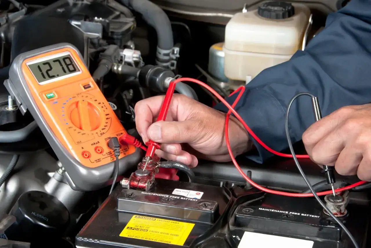 Mechaniker prüft Autobatterie mit Multimeter. Mögliche Symptome eines defekten Magnetschalters werden untersucht.
