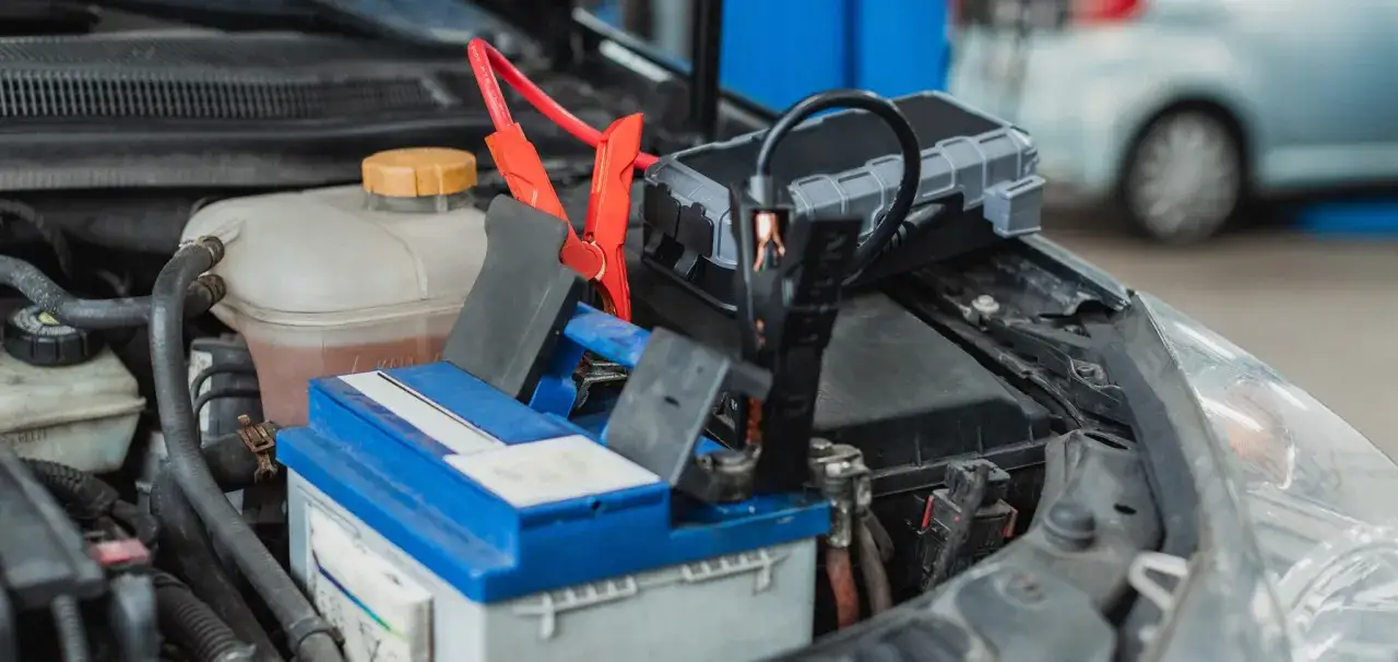 Starthilfe geben: Ein Auto-Batterie-Booster mit roten und schwarzen Klemmen ist an der Autobatterie angeschlossen.