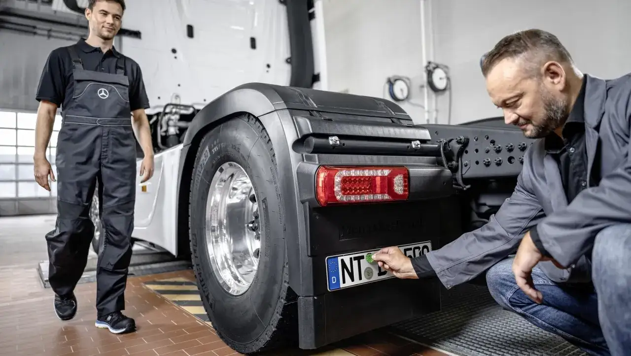 Mechaniker pr&uuml;ft Lkw-R&uuml;cklicht. Ein Kollege beobachtet, w&auml;hrend der Motor ruckelt und die Inspektion l&auml;uft.