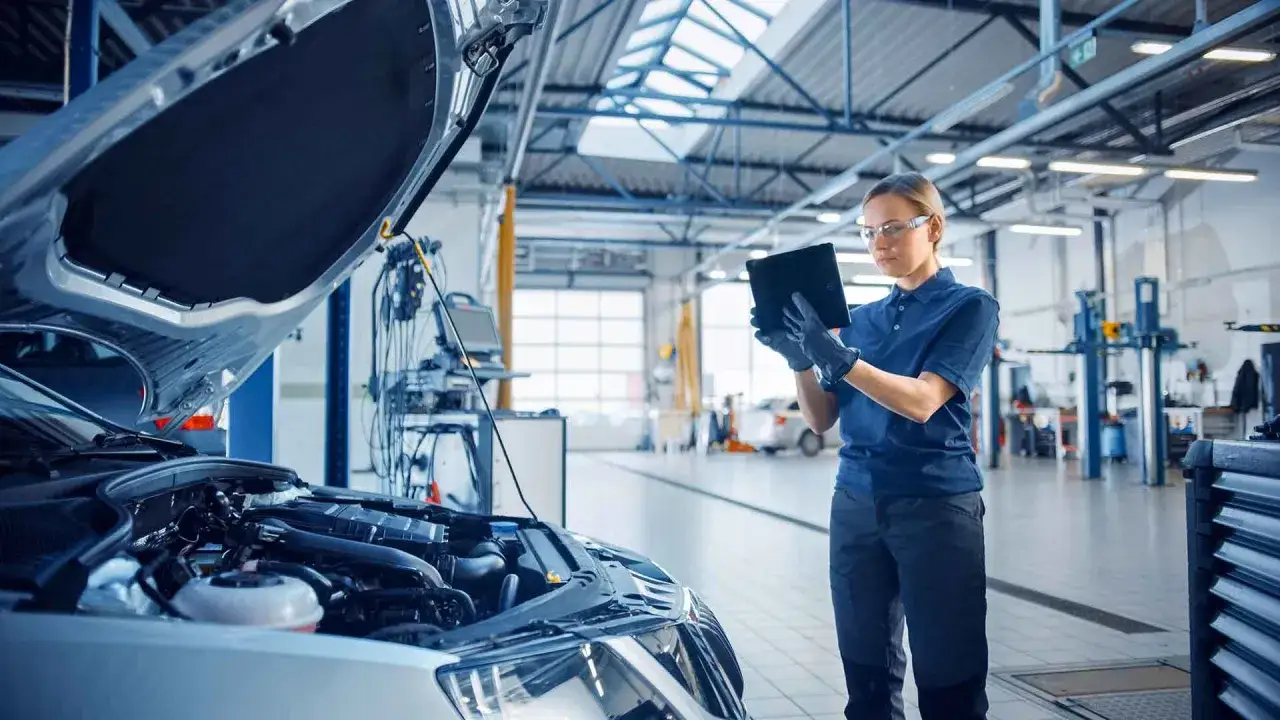 Mechanikerin pr&uuml;ft mit Tablet den Motor eines Firmenwagens. UVV-konforme Wartung im Autohaus.