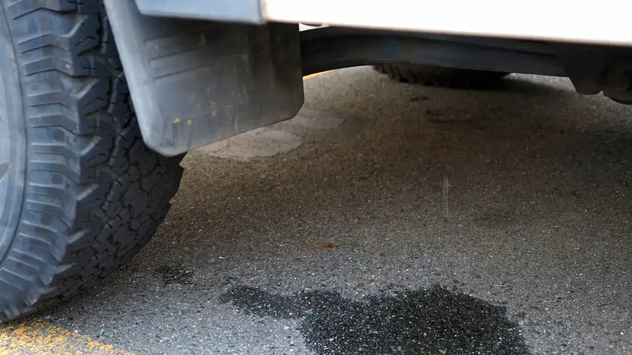 Ein Auto tropft Wasser nach der Fahrt. Die nasse Stelle auf dem Asphalt deutet auf ein Problem hin.