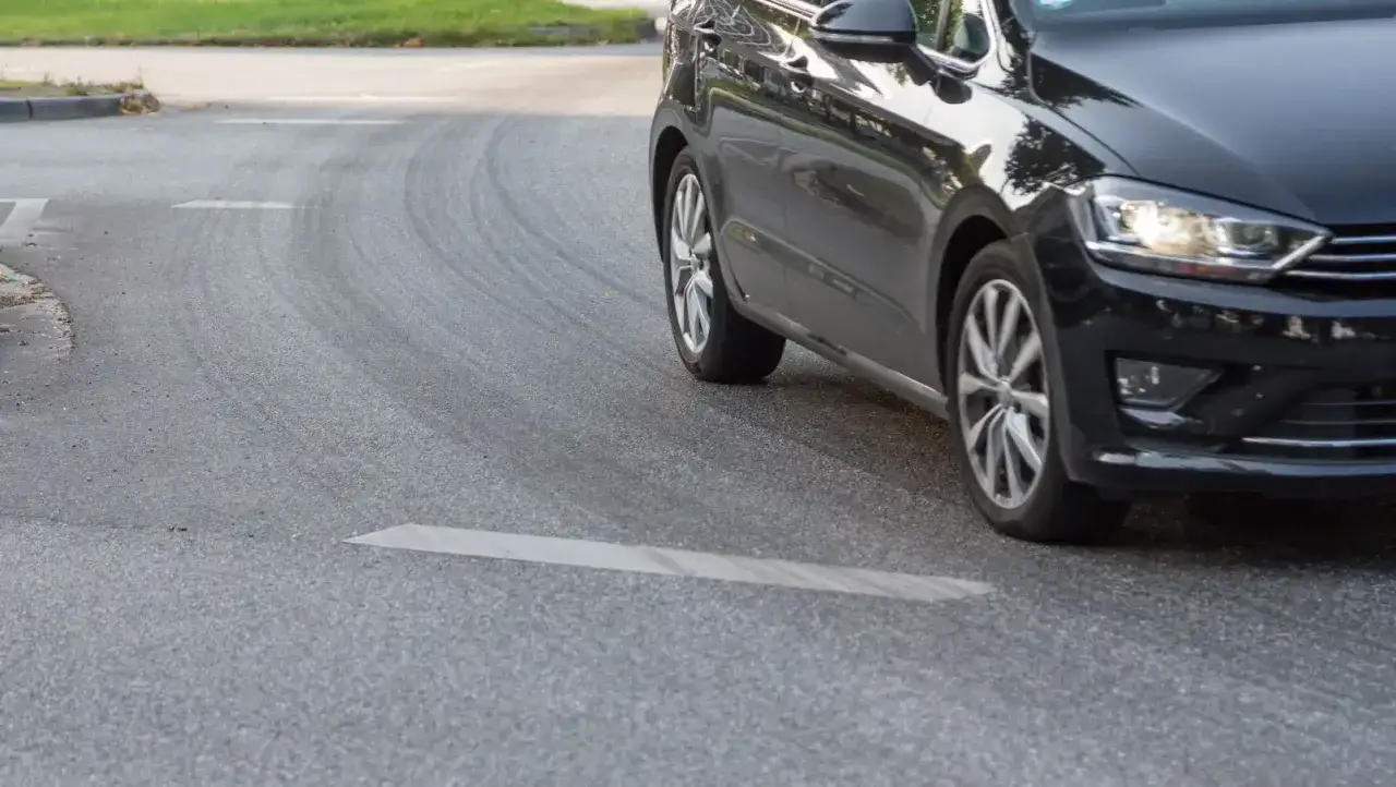 Schwarzes Auto quietscht beim Fahren in einer Kurve auf nasser Stra&szlig;e. Reifen hinterlassen Spuren.