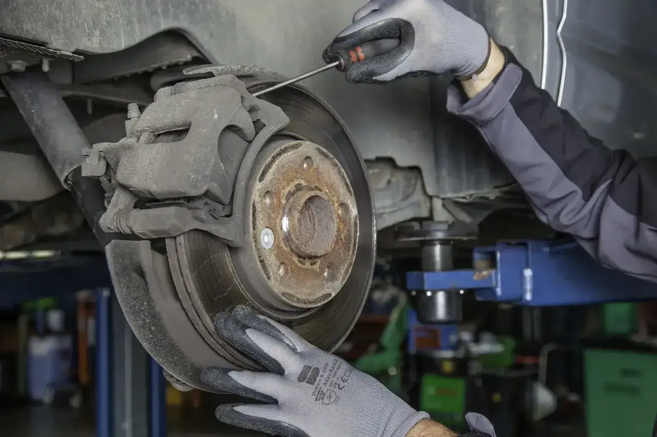 Mechaniker pr&uuml;ft abgefahrene Bremsen an einem Auto. Ein Schraubenzieher wird benutzt, um die Bremsscheibe zu inspizieren.