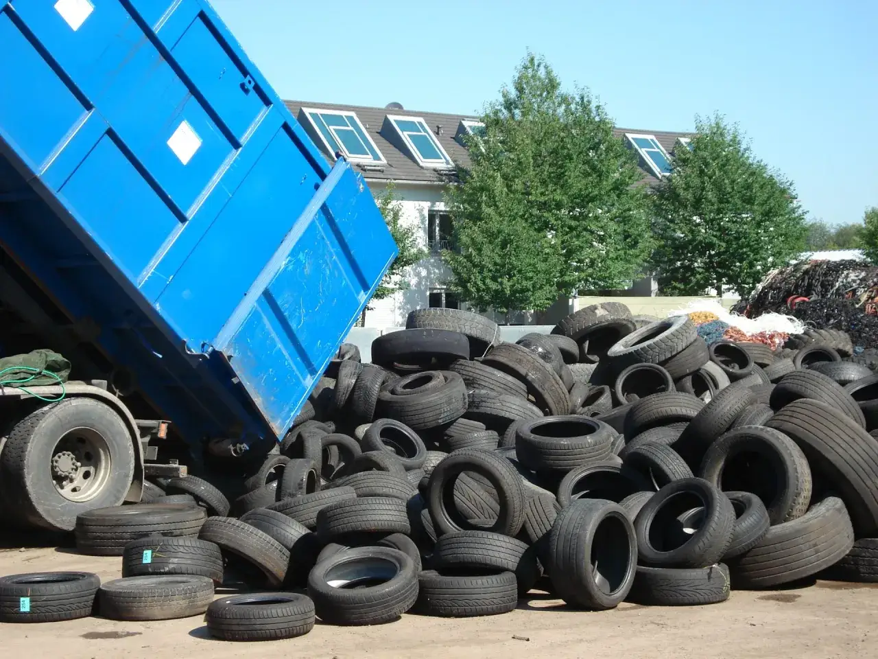 Ein blauer LKW-Container kippt Reifen ab. Ein gro&szlig;er Haufen alter Reifen wartet darauf, entsorgt zu werden.