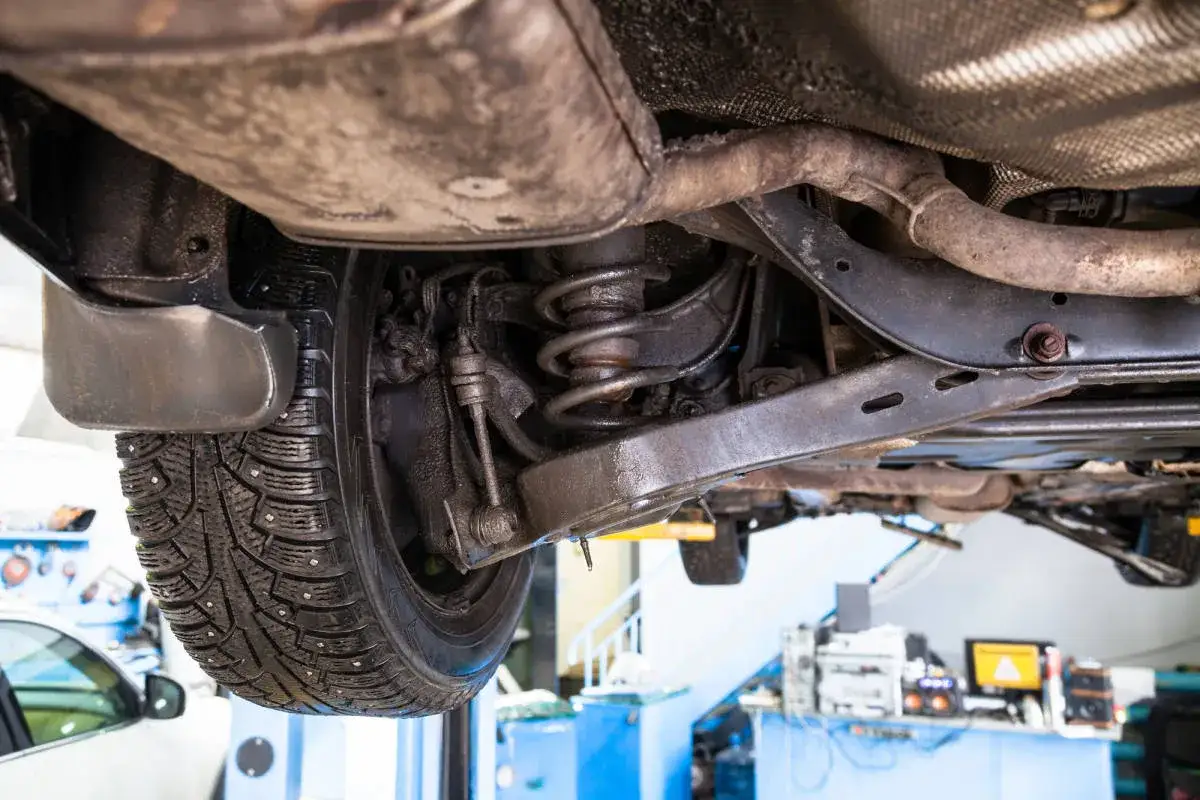 Unterseite eines Autos mit sichtbarer, gebrochener Feder. Der Reifen ist mit Spikes versehen.