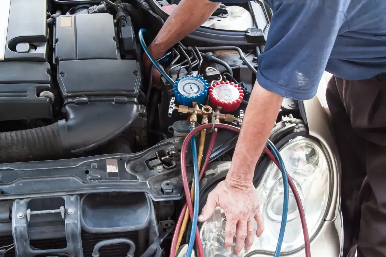 Mechaniker pr&uuml;ft mit Manometern, ob die Klimaanlage defekt ist. Bunte Schl&auml;uche f&uuml;hren zum Motorraum.