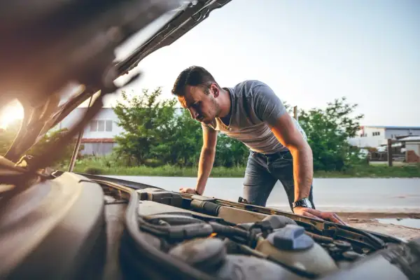 Mann beugt sich über den offenen Motorraum, weil der Motor stottert. Er sucht nach der Ursache des Problems.