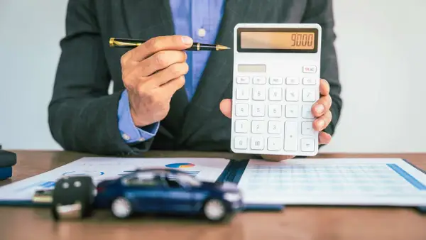 Mann mit Stift und Taschenrechner, der 9000 anzeigt. Auf dem Tisch liegen ein Auto-Schlüssel und ein Modellauto, was auf die **Erstattung Minderkilometer Leasing** hindeutet.