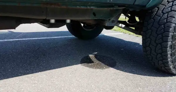 Ein Auto tropft Wasser nach der Fahrt. Eine Pfütze bildet sich auf dem Asphalt unter dem Fahrzeug.