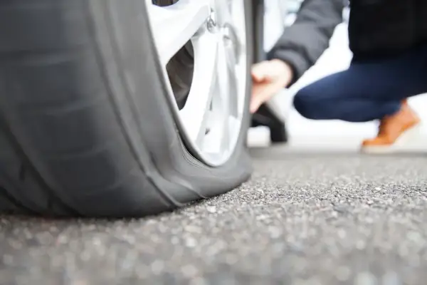 Platter Reifen am Auto. Eine Person kniet daneben und prüft den Schaden. Was tun bei reifen platt?
