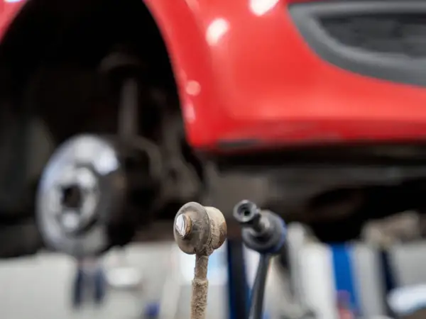 Zwei Koppelstangen liegen vor einem roten Auto. Die Koppelstange ist ein wichtiges Bauteil für die Fahrstabilität.