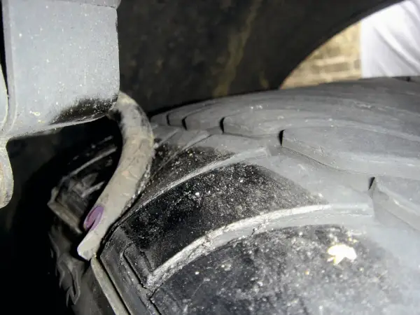 Nahaufnahme eines Reifens mit sichtbaren Rissen und einer verbogenen Metallfeder. Ein **feder gebrochen auto**-Problem, das dringend behoben werden muss.