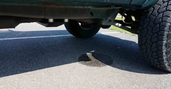 Ein Auto tropft Wasser nach der Fahrt. Eine Pfütze bildet sich auf dem Asphalt unter dem Fahrzeug.